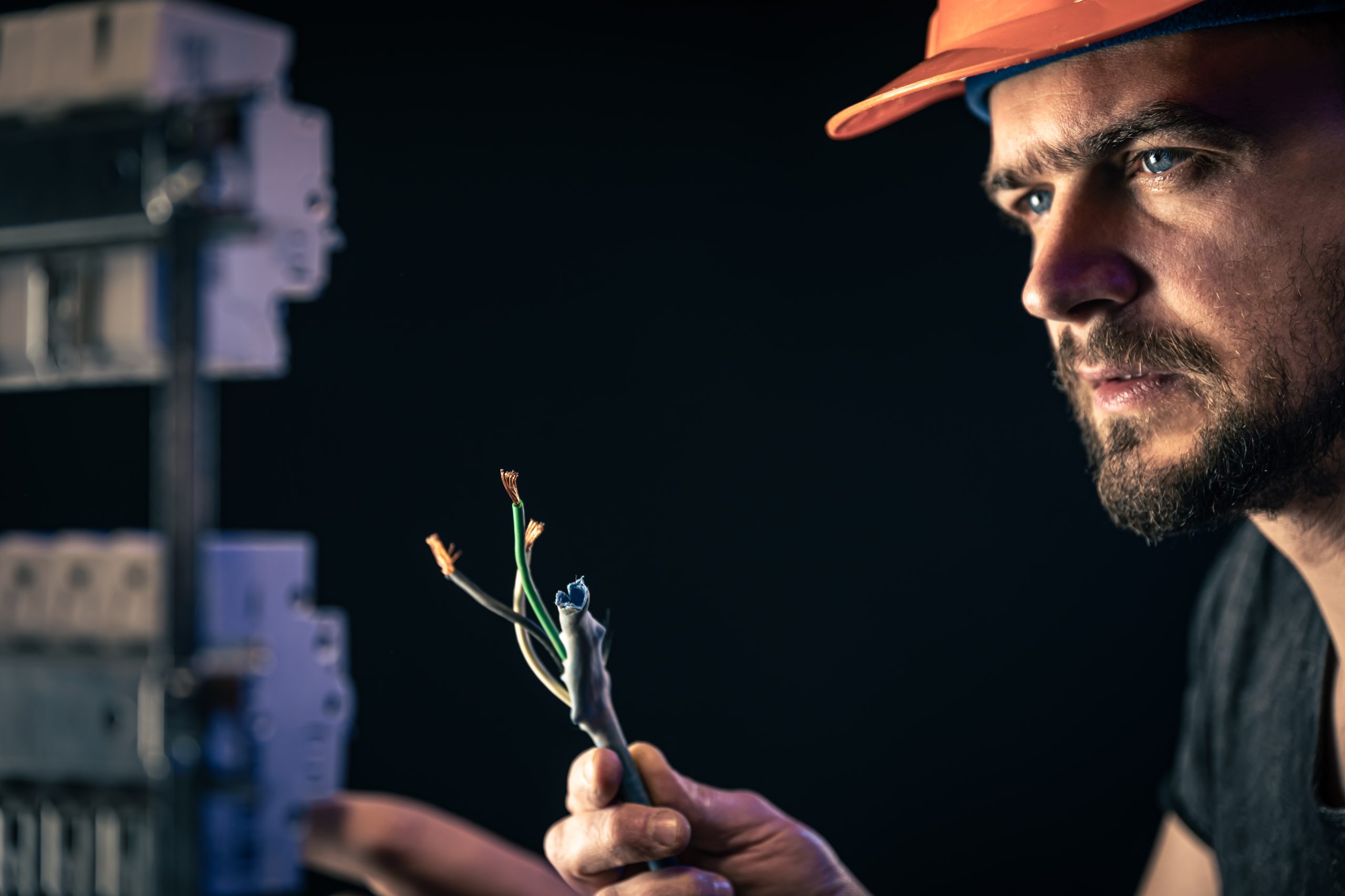 A male electrician works in a switchboard with an electrical connecting cable in New York